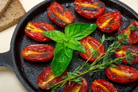 Oven baked cherry tomatoes with basil and thyme on a cast iron skillet