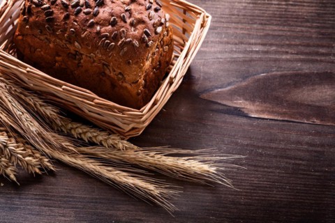Crusty bread with seeds in wicker basket Wheat ears on vintage pine wooden board Food and drink concept