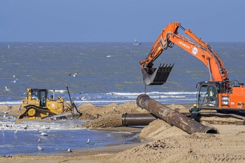 Bulldozer and hydraulic excavator installing pipeline during sand replenishment