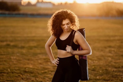 Curly girl runner with a yoga mat stands at sunset on the lawn