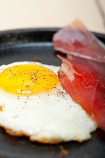 Fried egg sunny side up with Italian tyrolean speck smoked ham on a skillet