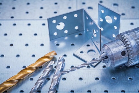 Drill with metal drills and drilled angle bars on a perforated metal background Design concept