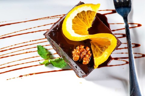 Fresh baked delicious chocolate and walnuts cake with slice of orance on top and mint leaf