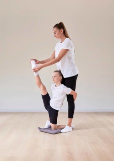 Beautiful female teacher helps a little girl stretch in a gymnastics class. The concept of education