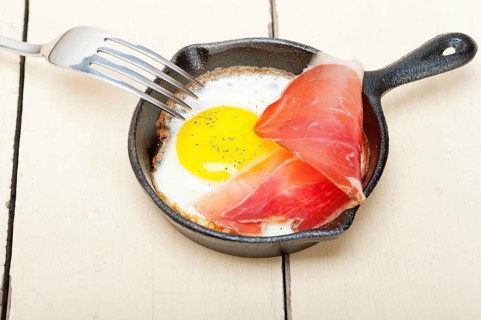 Fried egg sunny side up with Italian tyrolean speck smoked ham on a skillet
