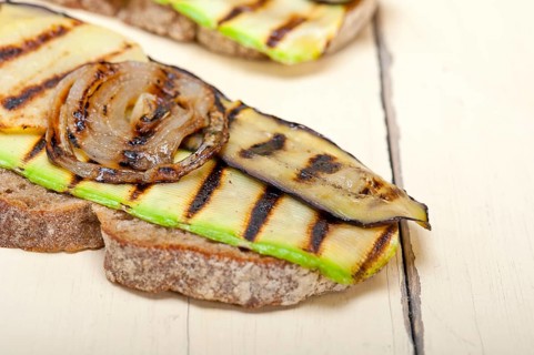 Grilled vegetables on rustic bread over wood table