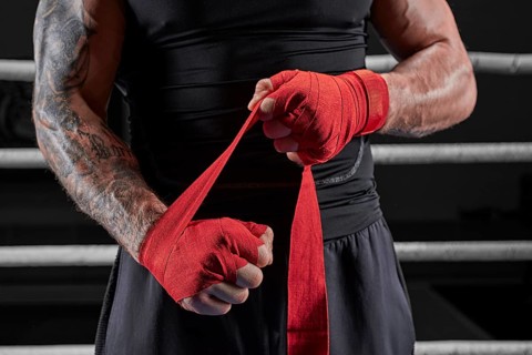 Red bandages on the hands of a kickboxer against the background of the ropes of the ring. The concept of mixed martial arts. MMA