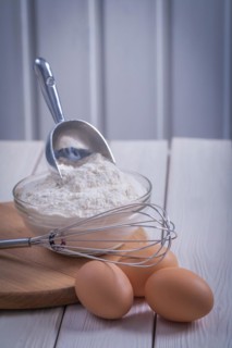 Corola egg bowl with flour scoop on white lacquered old wooden board Food and drink concept