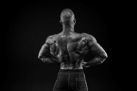 Silhouette of a strong bodybuilder. View from the back. Confident young fitness athlete with a powerful body and perfect abs. Black and white photography. Dramatic light
