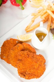 Classic breaded Milanese veal cutlets with french fries and vegetables on background