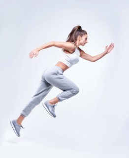 Sports woman runner on a white background. Photo of an attractive woman in fashionable sportswear. Dynamic movement. Side view. Sports and healthy lifestyle. Mixed media