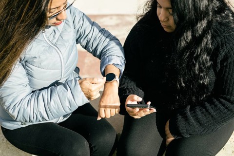 Two beautiful long hair latin women synchronizing data on smart phone and smart watch