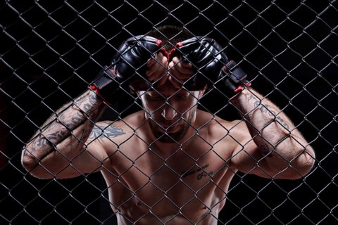 Dramatic image of a mixed martial arts fighter standing in an octagon cage. The concept of sports