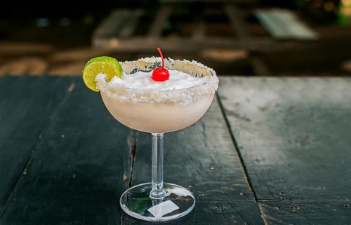 Frozen coconut cocktail with cherry on top on wooden table. Coconut margarita with cherry on wooden table