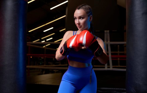 Image of a powerful sportswoman wrestler. Posing in a blue tracksuit and red boxing gloves. The concept of wrestling and boxing. Mixed media
