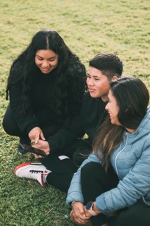 Three individuals of Hispanic-Latino ethnicity sitting on the lush green grass of a park