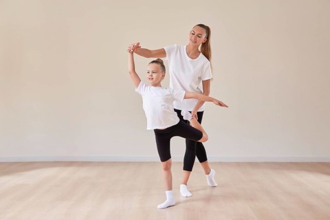 Beautiful woman teacher and a little girl perform dance movements in a bright studio. The concept of education