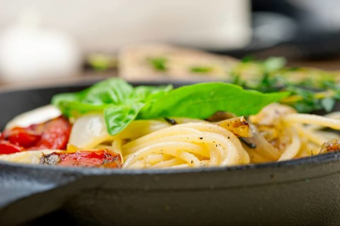 Italian spaghetti pasta with baked tomatoes basil and thyme sauce on a cast iron skillet