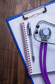Medical stethoscope with purple tubes on clipboard with biros and vintage wooden board