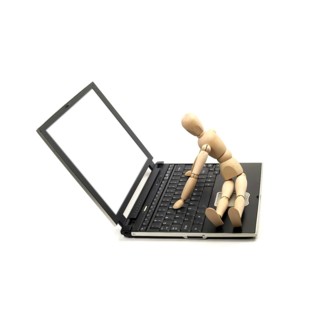 Wood mannequin sitting on a laptop isolated on white background
