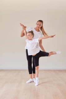 Beautiful woman teacher and a little girl perform dance movements in a bright studio. The concept of education