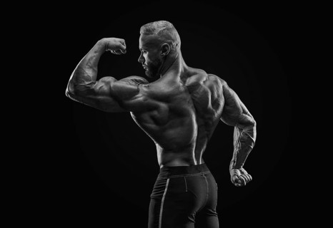 Silhouette of a strong bodybuilder. View from the back. Confident young fitness athlete with a powerful body and perfect abs. Black and white photography. Dramatic light