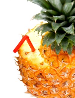 Ripe vivid pineapple with red straw over white background