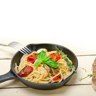 Italian spaghetti pasta with baked tomatoes basil and thyme sauce on a cast iron skillet