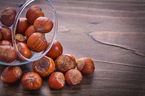 Horizontal version Stack of hazelnuts in glass bowl on vintage wooden board Food and drink still life
