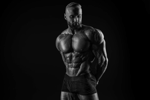 Silhouette of a strong bodybuilder. Confident young fitness athlete with a powerful body and perfect abs. Black and white photography. Dramatic light. Mixed media