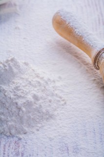 Small pile of white natural flour and wooden rolling pin in vertical version