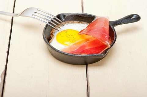 Fried egg sunny side up with Italian tyrolean speck smoked ham on a skillet