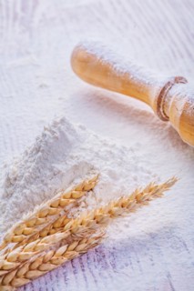 Wheat ears on a pile of white flour and a wooden rolling pin