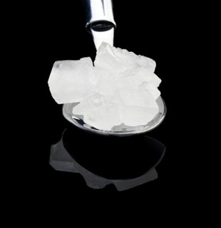 Crystal sugar on a spoon over black reflective surface background