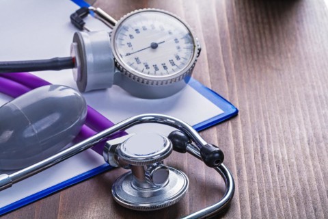 Medical stethoscope blood pressure monitor on clipboard with blanc sheet of paper and vintage wooden board