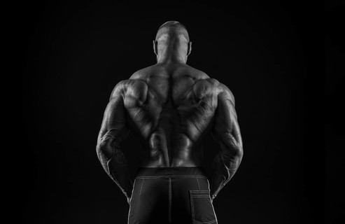 Silhouette of a strong bodybuilder. View from the back. Confident young fitness athlete with a powerful body and perfect abs. Black and white photography. Dramatic light