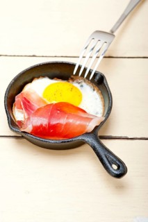 Fried egg sunny side up with Italian tyrolean speck smoked ham on a skillet