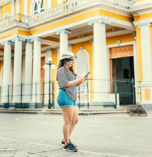 Lifestyle of tourist woman texting with phone on the street of square. Beautiful young travel woman with hat using cell phone on the street of Granada Nicaragua