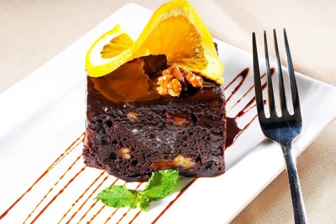 Fresh baked delicious chocolate and walnuts cake with slice of orance on top and mint leaf