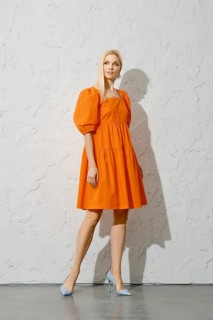 Stylish adult woman in overknee orange sundress posing near white textured wall