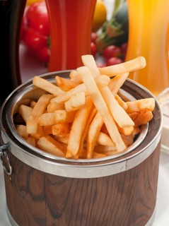 Fresh french fries on a wood bucket with selection of beers and fresh vegetables on background