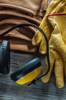 Leather safety gloves tool belt earmuffs on wooden board