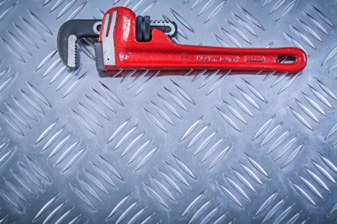 Adjustable monkey spanner on channeled metal background construction concept