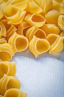 Heap of raw shell macaroni on blue background food and drink concept