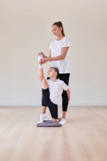 Beautiful female teacher helps a little girl stretch in a gymnastics class. The concept of education