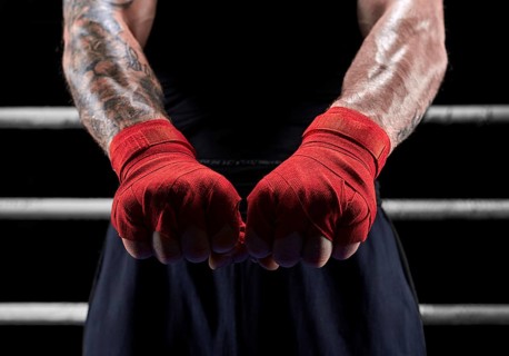 Red bandages on the hands of a kickboxer against the background of the ropes of the ring. The concept of mixed martial arts. MMA