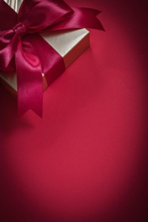 Wrapped giftbox with tied bow on red background holidays concept