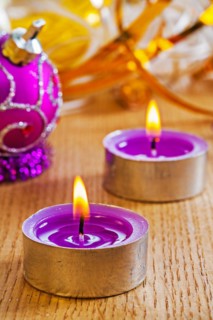 Two small glowing candles and Christmas baubles on a wooden board