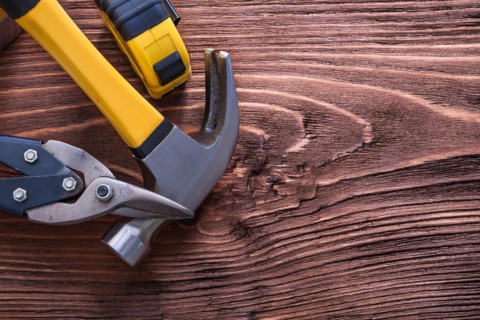Claw hammer pliers and tape measure on wooden panel construction concept