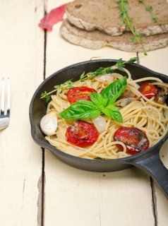 Italian spaghetti pasta with baked tomatoes basil and thyme sauce on a cast iron skillet